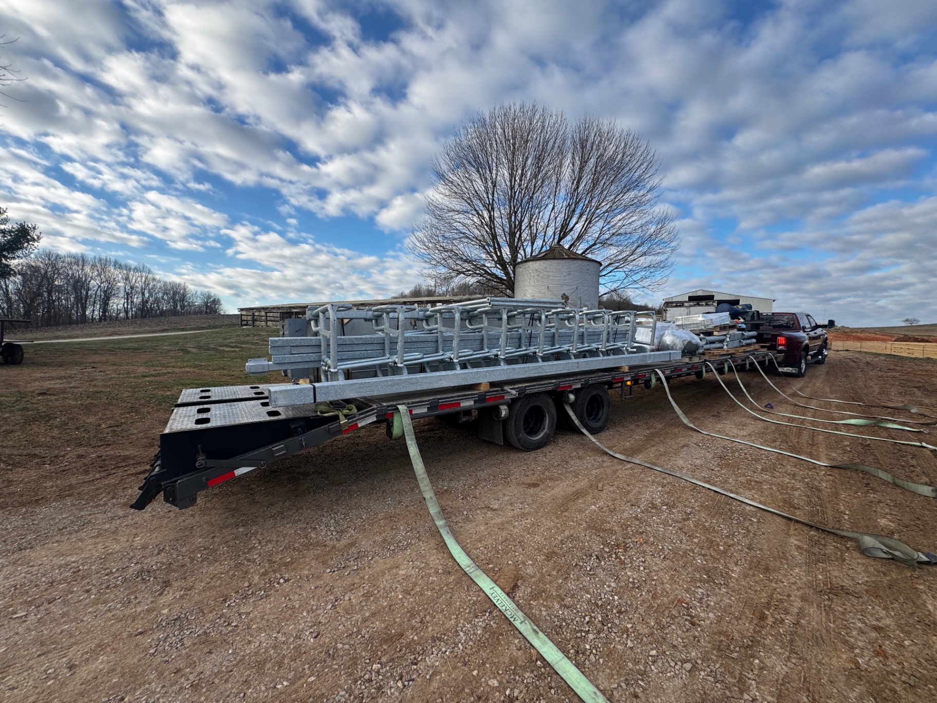 Construction equipment secured on flatbed with chains and straps, yard setting