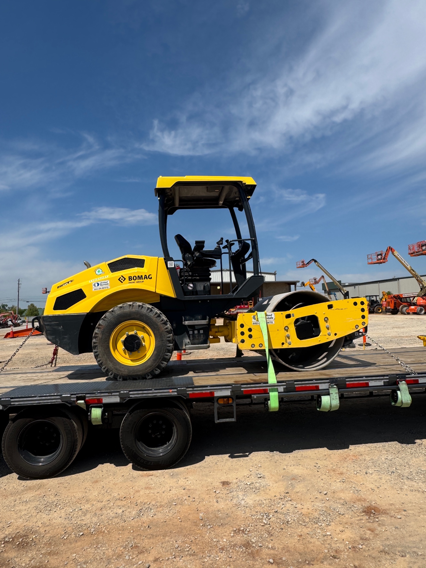 Heavy equipment loaded on flatbed trailer at job site, overcast sky, industrial setting